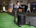 Focused middle aged woman in sportswear pushing heavyweight plates on prowler slider in gym