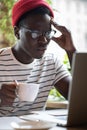 Focused millennial Black man student in stripped t-shirt wear glasses, watching educational webinar on laptop, remotely online Royalty Free Stock Photo