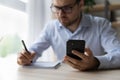 Focused millennial business man using mobile phone and taking notes Royalty Free Stock Photo