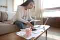 Focused millennial female sitting on couch analyzing monthly outgoings