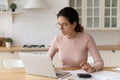 Focused millennial woman in eyeglasses paying bills online.