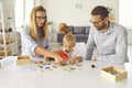 Focused mom, dad and toddler son play and compose words from scattered colored letters.