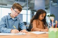 Focused multiracial students kids writing down data into notebook while sitting at table