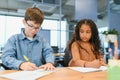 Focused multiracial students kids writing down data into notebook while sitting at table