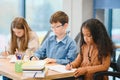 Focused multiracial students kids writing down data into notebook while sitting at table