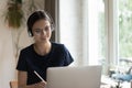 Focused positive young student girl in eyeglasses, headphones writing notes