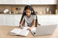 Focused pre teen schoolkid girl in headphones studying from home