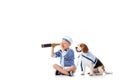 Preschooler child in sailor costume looking in spyglass while sitting with beagle dog on white