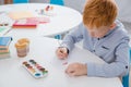 focused preschooler red hair boy drawing picture at table