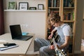 Focused preteen girl learning to play the guitar in virtual meeting together with teacher in video conference.