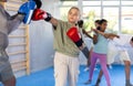 Preteen girl in boxing gloves practicing punches on mitts with coach