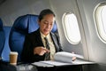 A focused mature Asian businesswoman reading and reviewing business reports during the flight Royalty Free Stock Photo