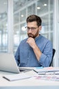 Focused professional using a laptop while thinking in a modern office setting Royalty Free Stock Photo