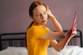 Focused redhead young woman with natural beauty applying powder or blusher on face with big makeup brush sitting on bed Royalty Free Stock Photo