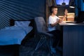 focused schoolboy wearing headphones uses laptop for distance learning at night. child raises his hand to answer lesson