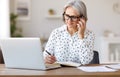 Focused senior business woman talking on mobile phone using laptop while working remotely at home Royalty Free Stock Photo