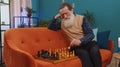 Focused senior grandfather man playing chess leisure board game alone, domestic activity at home