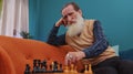 Focused senior grandfather man playing chess leisure board game alone, domestic activity at home