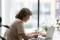 Focused senior homeowner, landlady reading paper document at laptop