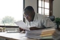 Focused serious african american businessman accountant analyst holding documents while using laptop computer screen Royalty Free Stock Photo