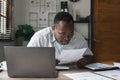 Focused serious african american businessman accountant analyst holding documents while using laptop computer screen Royalty Free Stock Photo