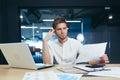 Focused and serious young man IT specialist, manager, businessman working on laptop and with documents in the office at the desk. Royalty Free Stock Photo