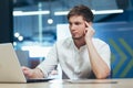 Focused and serious young man working on laptop and with documents in the office at the desk. Holds his head, He thinks Royalty Free Stock Photo