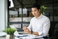 Focused Asian businessman reading business online documents on his laptop at his desk Royalty Free Stock Photo