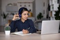Focused smiling Indian student girl in headphones studying from home