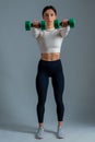 Sporty girl doing dumbbell front raise with both hands on grey background Royalty Free Stock Photo