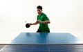 Focused table tennis serve from Asian player in vibrant green sportswear in motion against white studio background