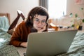 Focused teen girl studying, watching online lecture, webinar, seminar at laptop lying in bed at home Royalty Free Stock Photo