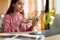 Focused teen girl using smartphone and laptop, studying online at home, chatting and checking social media