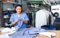 Focused woman dry-cleaning worker checking clean clothes Royalty Free Stock Photo