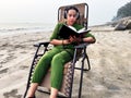 Focused woman with headphones reading book while sitting on a deck chair at a sandy beach location Royalty Free Stock Photo