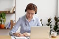 Focused woman in headphones using laptop, writing notes Royalty Free Stock Photo