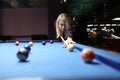 Focused woman hits white ball leaning above blue pool table Royalty Free Stock Photo