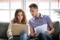 Focused worried couple paying bills online on laptop with document