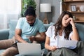 Focused worried couple paying bills online on laptop with documents sitting together on sofa at home, serious confused man and Royalty Free Stock Photo