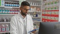 A focused young african american man with beard wearing glasses and a white coat analyzing data on a tablet in a pharmacy Royalty Free Stock Photo