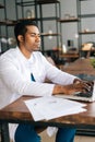 Focused young African male doctor in white coat working typing on laptop computer sitting at desk. Royalty Free Stock Photo