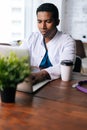 Focused young African male doctor in white coat working typing on laptop computer sitting at desk. Royalty Free Stock Photo