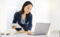 Focused young asian businesswoman using a digital tablet device and laptop while planning notes at a desk in an office Royalty Free Stock Photo