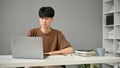 A focused young Asian man browsing the internet and using his laptop in his home office Royalty Free Stock Photo