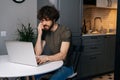 Focused young bearded business man talking on smartphone sitting at table with laptop in kitchen with modern interior Royalty Free Stock Photo