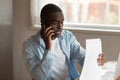 Focused young black man holding documents, calling to financial advisor. Royalty Free Stock Photo