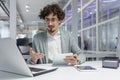 Focused young businessman in office environment working on laptop and holding notebook Royalty Free Stock Photo