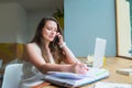 Focused Young businesswoman making notes in notebook while talking on mobile phone and working on laptop in cafe