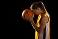 Focused young Caucasian female basketball player cradles a basketball in a studio setting on a black