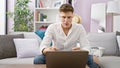 Focused young caucasian man sitting indoors on sofa, using laptop, engrossed in online technology at home! handsome male, Royalty Free Stock Photo